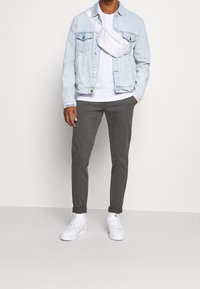 Jeansjacka i ljusblått, vit t-shirt, grå byxor och vita sneakers. Inkluderar en vit axelremsväska som bärs på axeln.