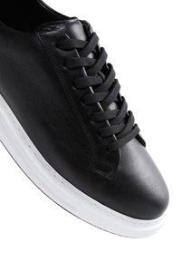 Sneaker in pelle nera con lacci neri piatti, punta tonda e suola in gomma bianca. Presenta una texture liscia e dettagli di cucitura ridotti al minimo.