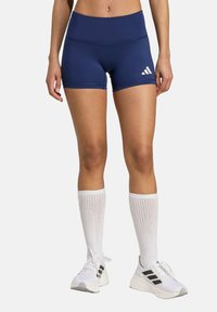 Mornarskoplave atletske kratke hlače s visokim pojasom, s bijelim Adidas logotipom. Nosene uz bijele čarape do koljena i bijele tenisice.
