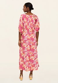 Rochie lungă, florală, roz, cu mâneci bufante și detaliu pliat la spate. Prezintă un model cu flori galbene și albe, dintr-un material ușor și fluid.