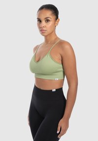 Top corto acanalado de color verde claro con tirantes finos, combinado con leggings negros de tiro alto. Presenta una pequeña etiqueta de la marca en el dobladillo inferior.