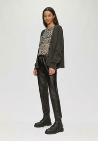 Szary, oversize kardigan z guzikami, wzorzysta przezroczysta bluzka, czarne spodnie z sztucznej skóry i czarne buty na sznurówki. Gładkie faktury i swobodny styl.