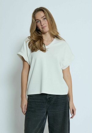 T-shirt bianco a maniche corte con scollatura a V, realizzato in tessuto morbido. Vestibilità rilassata con risvolti, abbinato a jeans grigi scuri.