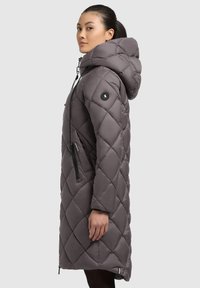 Gray quilted long puffer coat with a hood, adjustable drawstring, side pocket, and black logo patch on the sleeve. Smooth, textured finish.