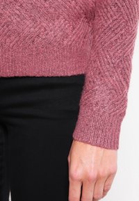 Maglione lavorato a maglia in un morbido misto lana rosa, caratterizzato da un motivo a spina di pesce testurizzato e polsini a costine, abbinato a tessuto nero.