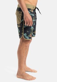 Boardshorts mit schwarzem Grund, tropischem Muster in Grün und Rot, hellbraunem Bund und einer Seitentasche. Leichter Stoff mit glatter Textur.