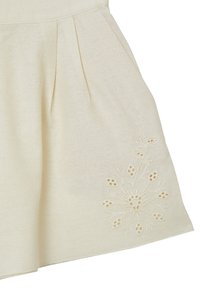 Jupe beige avec des plis et des détails de broderie florale près de l'ourlet sur le côté droit, fabriquée en tissu texturé.