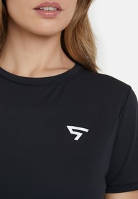 Črna atletska majica iz gladkega materiala. Ima bel logo na levem prsnem delu. Okrogla izreza in kratki rokavi.