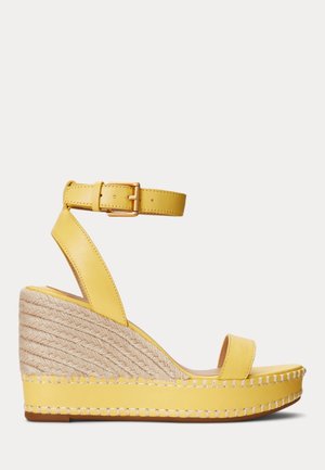 Sandale compensée en cuir jaune avec des détails en jute tressé sur le talon, une bride de cheville réglable et un design ouvert.