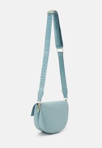 Crossbody taška Valentino v světle modré kůži, s kulatým tvarem, zavíráním na klopu a nastavitelným páskem s logem. Zlaté kovové detaily.