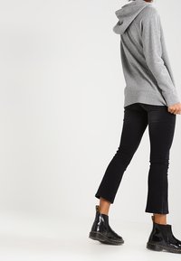 Felpa grigia con cappuccio e vestibilità comoda, abbinata a jeans neri svasati e stivaletti neri lucidi con dettagli gialli.