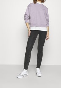 Lilac sweatshirt with ribbed cuffs, layered over a white shirt. Paired with black skinny jeans and white sneakers with eyelet detailing.
