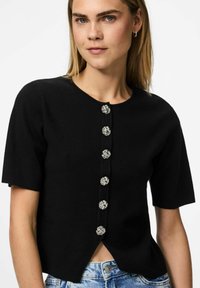 Melnā adītā īso piedurkņu blūze ar apaļu kakla izgriezumu, sudraba puķu formas pogām priekšpusē un nedaudz izliekta apakšmalu.