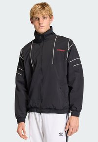 Black windbreaker jacket featuring elastic cuffs and hem, white accent lines, and a small red Adidas logo on the chest.