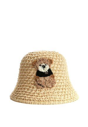 Sombrero de cubo beige de ganchillo con un pequeño parche de oso de peluche marrón que lleva una camisa negra en el frente.