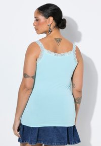 En ljusblå linne med spetskant vid halsringningen och axelbanden, med en mjuk textur, i kombination med en jeanstul. 