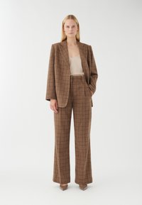 Brun ternet jakkesæt med vidde bukser og en struktureret blazer, suppleret med en beige top og spidse hæle.