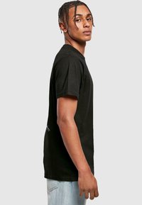 Black cotton t-shirt with short sleeves and a crew neckline, featuring a minimalist design with grey accents on the back. Standard fit.