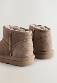 Bruna mockakängor med mjukt foder i päls och platta gummisulor. Har stickade sömmar, rundad topp och ett kort skaft.