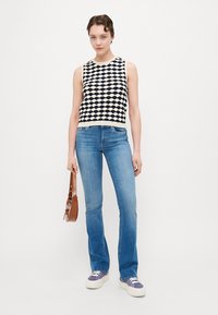 Strikket ærmeløs topp med et marineblått og kremmønstret bølgedesign, parret med lyseblå flagrende jeans og hvite sneakers. Brun skulderveske inkludert.