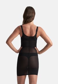 Indumento modellante nero con spalline regolabili, texture liscia e dettagli in panneli trasparenti. Il design presenta un corsetto aderente e una gonna.