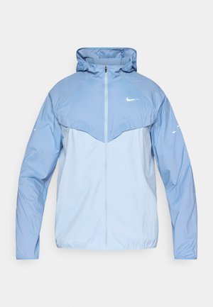 Giacca con zip azzurro chiaro realizzata in tessuto leggero, con cappuccio, pannello superiore a contrasto e logo Nike discreto sul petto.