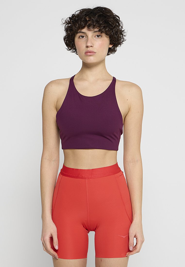 Top corto atlético morado con escote redondo, combinado con pantalones cortos de talle alto rojos brillantes que presentan una textura suave y un diseño elegante.
