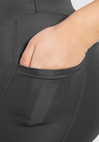 Pantaloni sportivi neri con una tasca laterale, caratterizzati da un tessuto liscio, un design aderente e cuciture a contrasto lungo le cuciture.