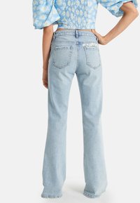 Jeans acampanados de mezclilla azul claro con una cintura alta, cinco bolsillos, costuras visibles y un sutil detalle floral en el bolsillo trasero.