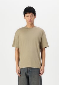 Khaki short-sleeve T-shirt made of soft cotton, featuring a crew neckline and relaxed fit, paired with dark denim pants.