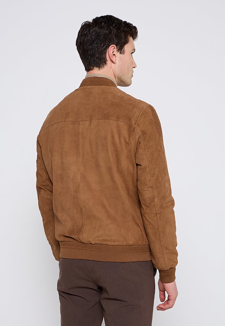 Brązowa kurtka bombowca z zamszu, z prążkowanym paskiem w talii, gładką fakturą i prostym, minimalistycznym wzornictwem. Cechuje się czystym krojem z tyłu.