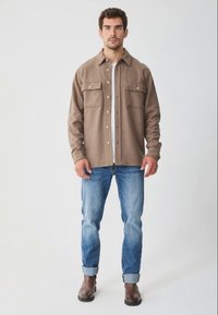 Braunes Hemdjacke aus Wollmix mit zwei Brusttaschen und Knopfverschluss, kombiniert mit hellblauen Jeans und braunen Lederstiefeln.