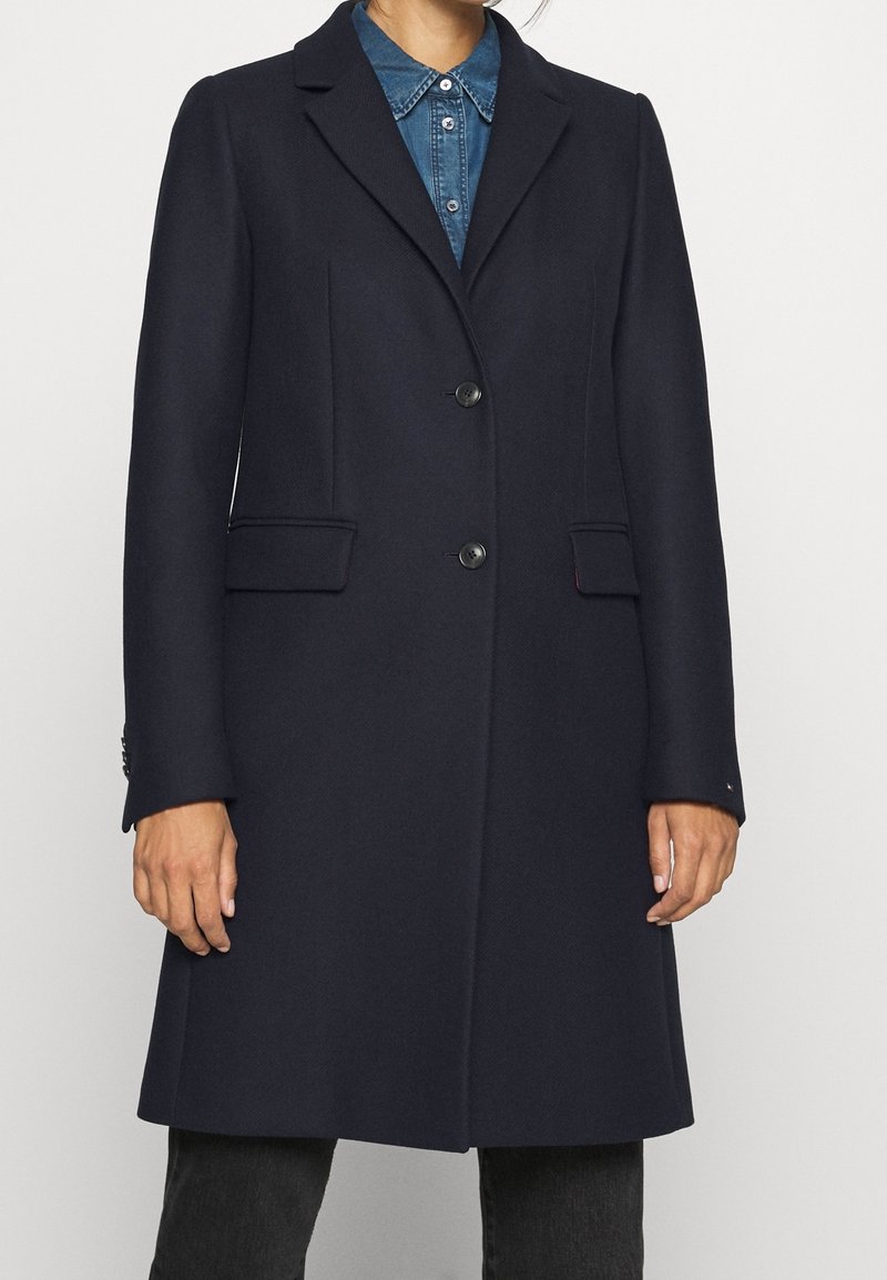 Marineblauwe wollen blend jas met omgeslagen revers, twee voorzakken, twee knopen en een getailleerde pasvorm, gecombineerd met een denim overhemd eronder.