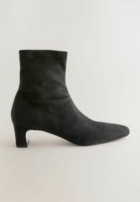Bottillon en suede noir avec un bout pointu et un talon bloc élégant, caractérisé par une texture lisse et une silhouette ajustée.