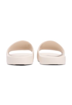 Par beige slip-on sandaler med brede forremme og flade såler, vist bagfra på en hvid baggrund.