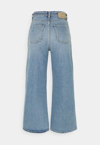 Jean en denim bleu clair à jambes larges avec deux poches arrière et une étiquette de marque en cuir marron sur la ceinture.