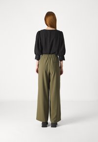 Svart bluse med puffede ermer og blonder, kombinert med olivengrønne vide bukser med elastisk midjebånd og baklomme.