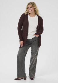 Cardigan tricoté bordeaux à l'avant ouvert, avec un motif texturé, associé à une chemise blanche et un jean gris à jambes larges. Talons en cuir verni noir.