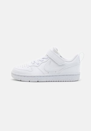 Biały niski sneaker z sznurowadłami i rzepem, perforowany nosek oraz nakrapiana podeszwa, prezentowany na prostym jasnym tle.