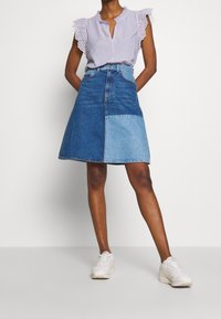 Farkkuhame korkealla vyötäröllä, jossa on väriblokki tummansinisen ja vaaleansinisen sävyissä. Lyhyt A-linjainen muoto, rispaantunut helma ja kestävä kangas.