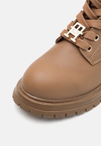 Brune skinn ankle støvel med teksturert overflate og polstret krage, med en gull hardware logo aksent og en robust såle med hakker.