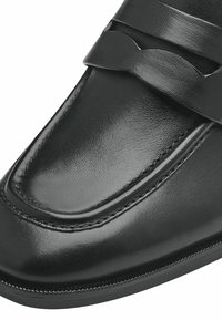 Svart lädersko med en slät yta, prydd med ett dekorativt band över ovandelen och noggrant stygn längs kanten.