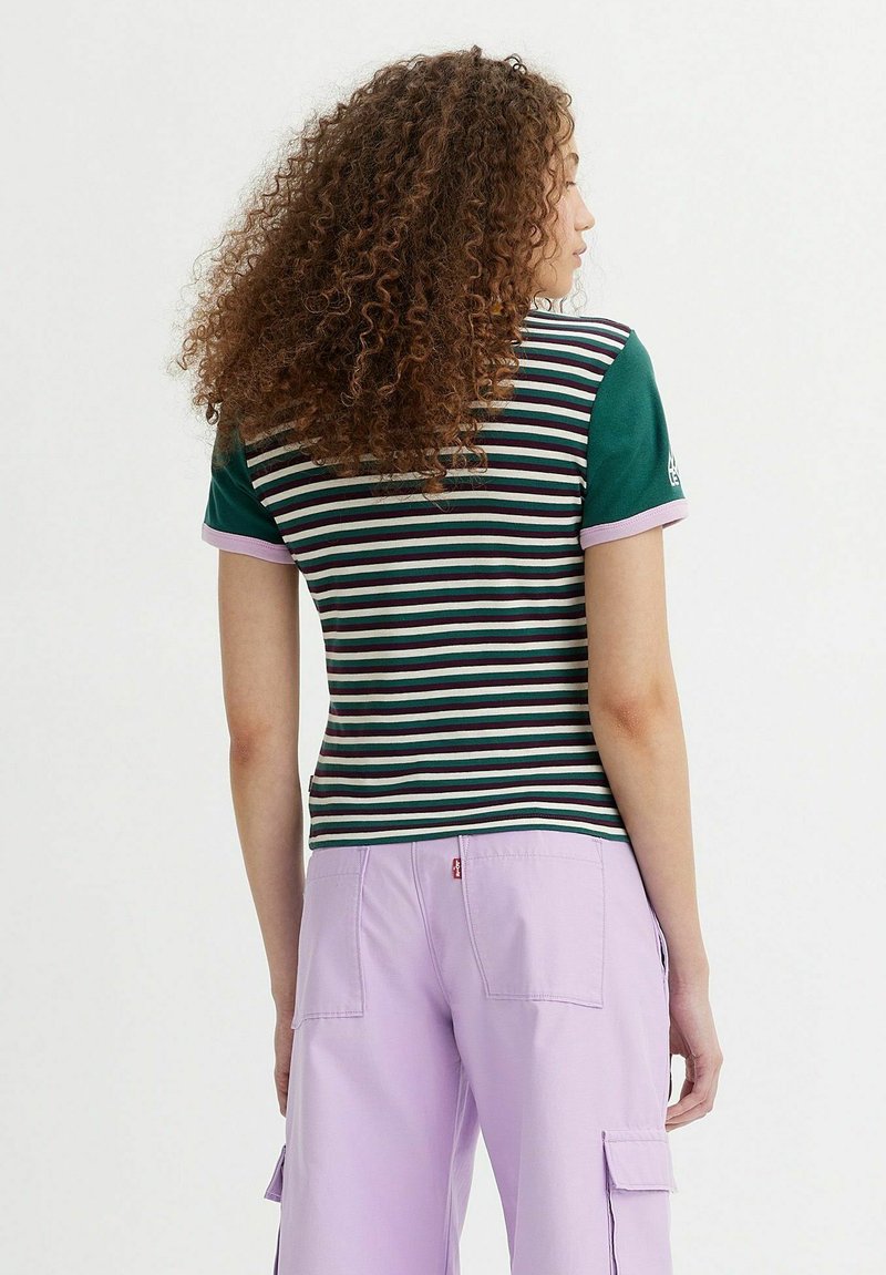 Gestreiftes Polohemd mit grünen Vorderärmeln, Lavendelmanschetten und tailliertem Design. Getragen mit lavendelfarbenen Cargo-Hosen, Rückansicht gezeigt.