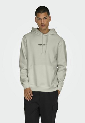 Light gray hoodie with drawstrings, a front kangaroo pocket, and black text reading “CURATED STAPLER.” Fabric appears smooth and soft.