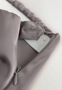 Close-up of a light grey garment corner with a zipper, button, and elastic band sewn inside for adjustable fit.