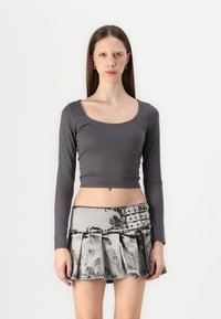Gray long-sleeve crop top with a scoop neckline; paired with a pleated, faded denim mini skirt featuring a buttoned waistband and side detailing.