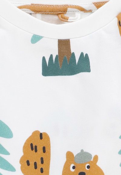 Camicia bianca in cotone con illustrazioni giocose di un orso che indossa un cappello, alberi e pietre in tonalità di arancione, verde e nero.