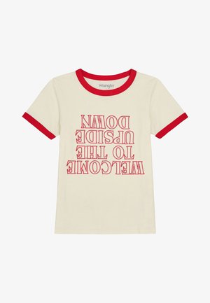 Camiseta de algodón color crema con cuello redondo y ribetes rojos, y mangas cortas. Texto frontal que dice "BIENVENIDO AL MUNDO AL REVÉS" en letras rojas y negrita.