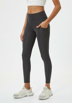 High-waisted, black leggings made from stretchy material with a pocket on the side, paired with light-colored athletic shoes.