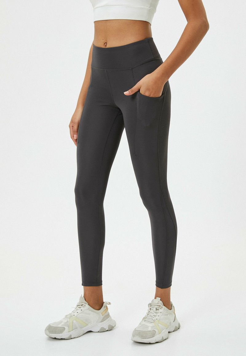 Leggings neri a vita alta realizzati in materiale elastico, con una tasca laterale, abbinati a scarpe da ginnastica chiare.